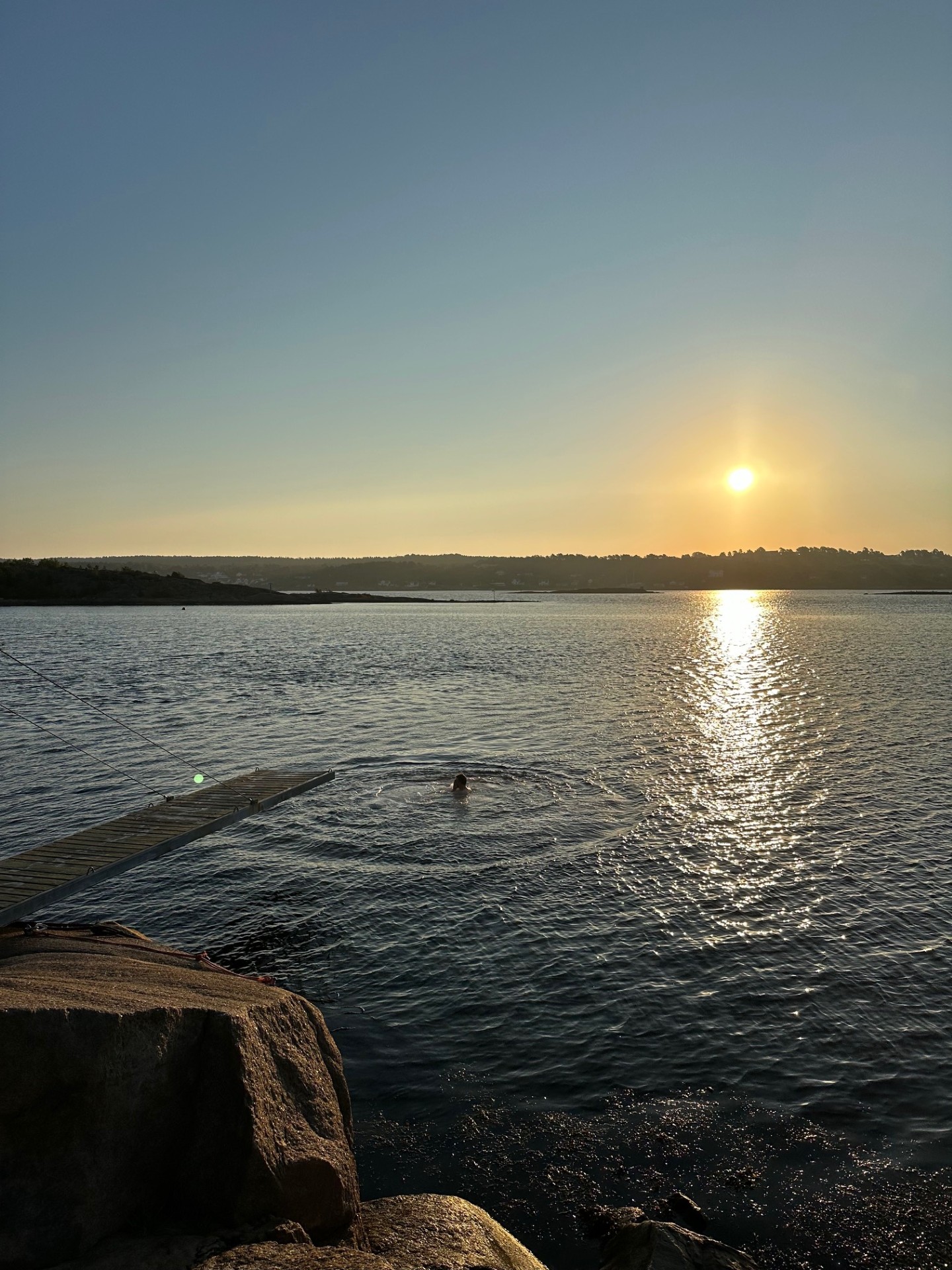 en person som svømmer i en vannmasse med en solnedgang i bakgrunnen
