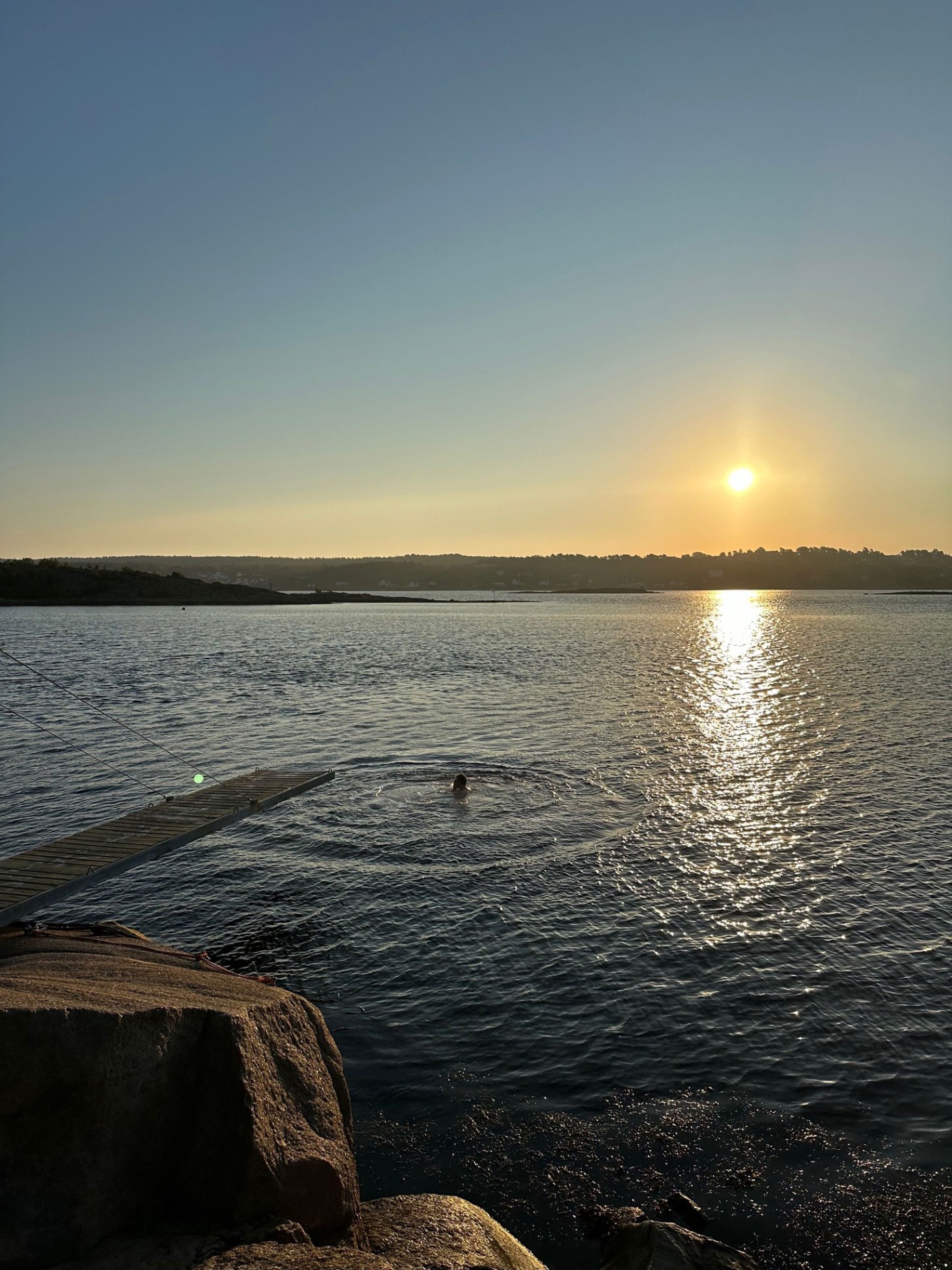 en person som svømmer i en vannmasse med en solnedgang i bakgrunnen