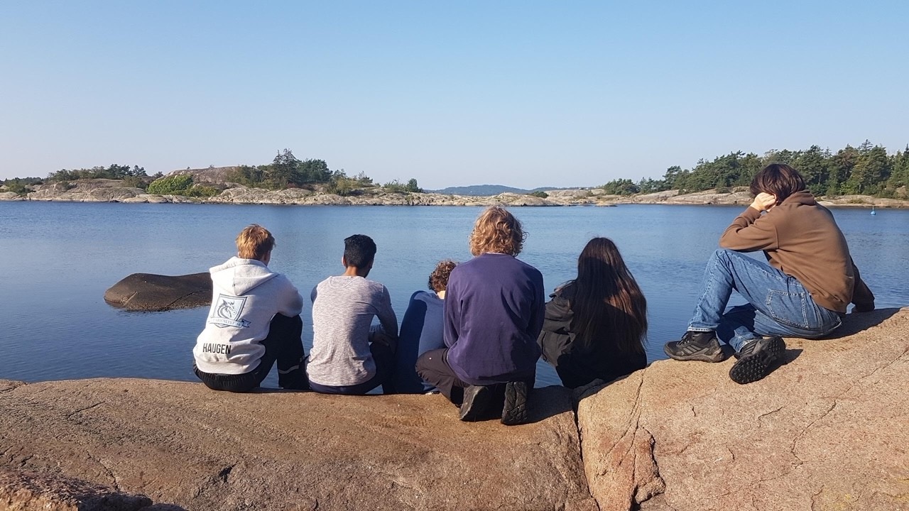 en gruppe mennesker som sitter på en stein og ser på vannet