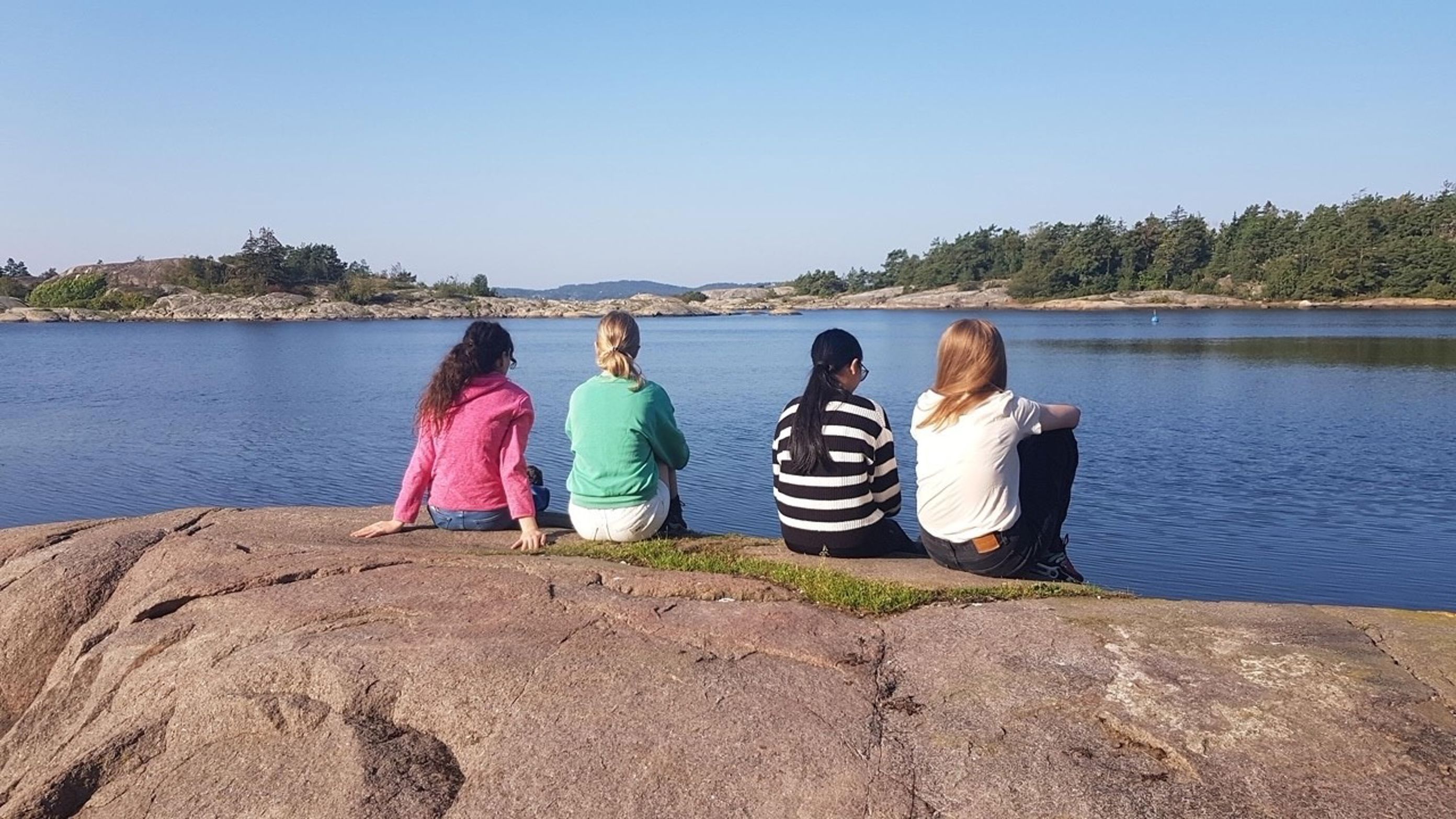 en gruppe personr som sitter på en stein ved en vannmasse