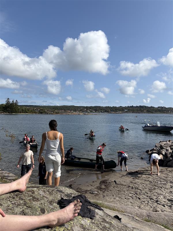 En gruppe mennesker på en steinete strand med båter i vannet