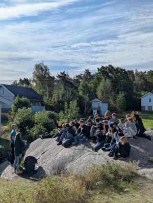 En gruppe mennesker som sitter på en stein foran et hus