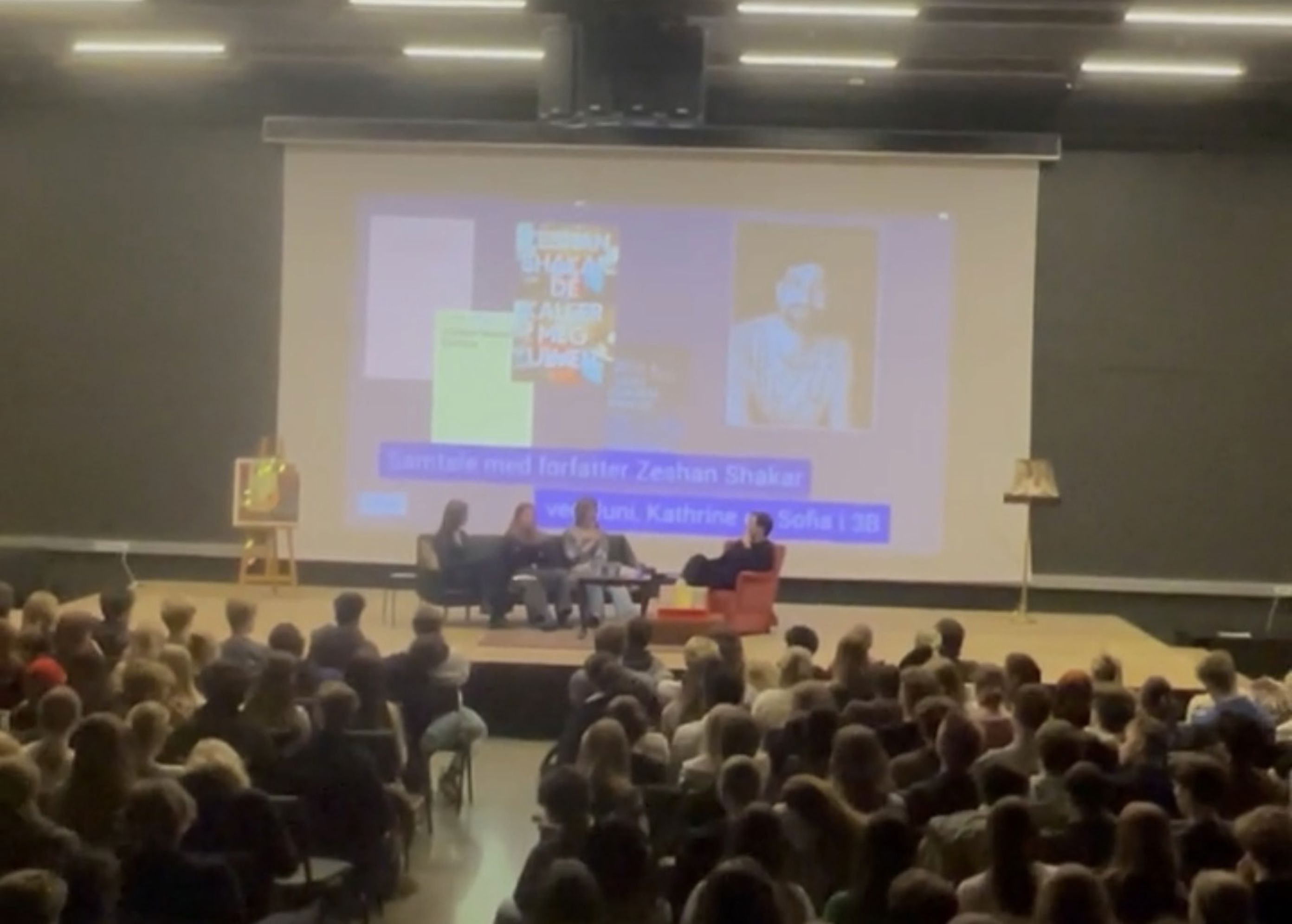 en gruppe mennesker som sitter i et rom med en projektorskjerm