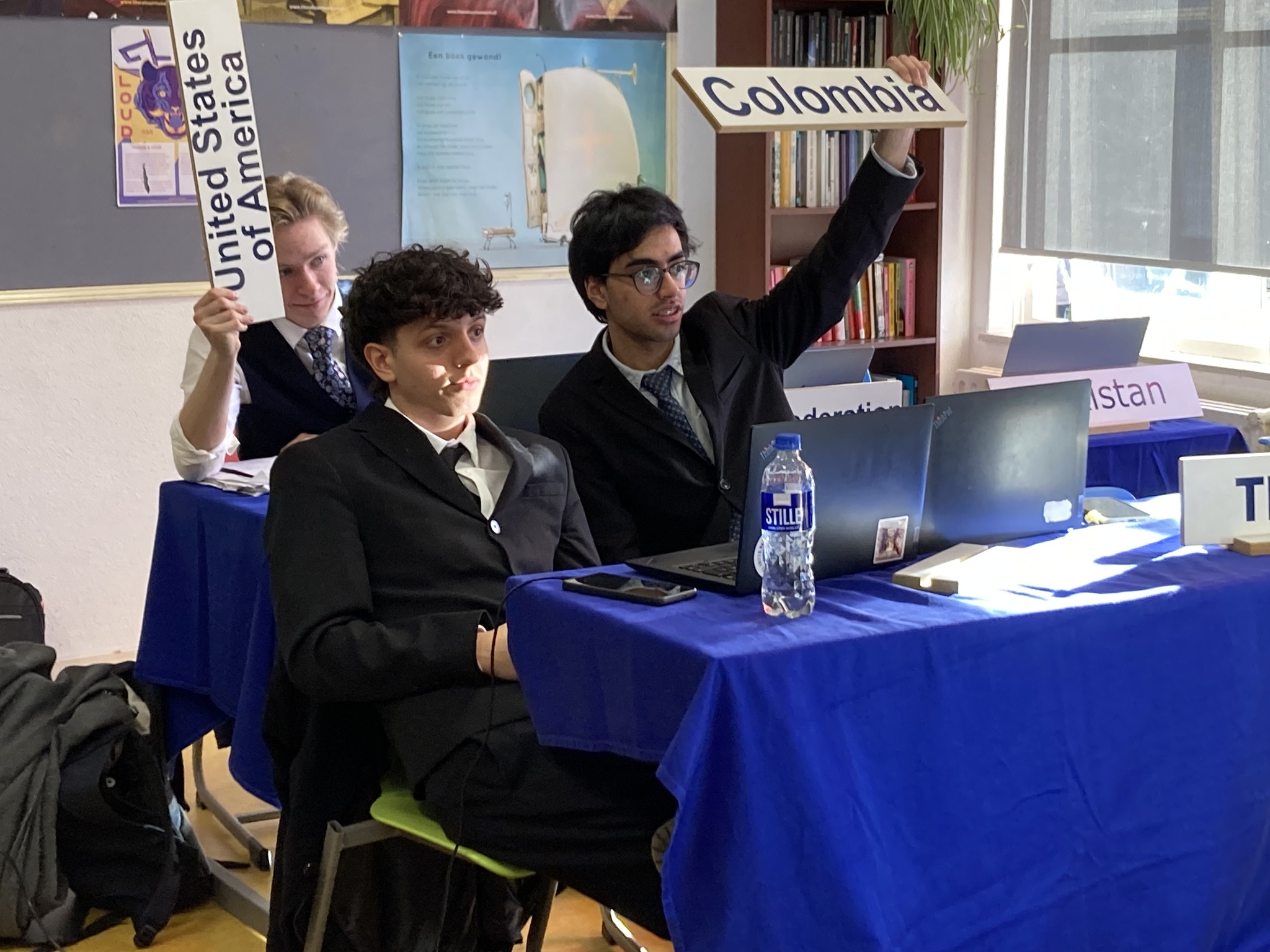 en gruppe mennesker som sitter ved et bord med bærbare datamaskiner og et skilt