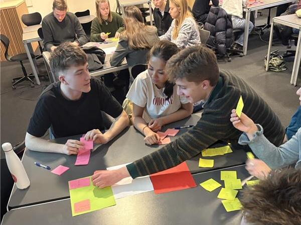 En gruppe mennesker som sitter ved et bord med fargerikt papir på