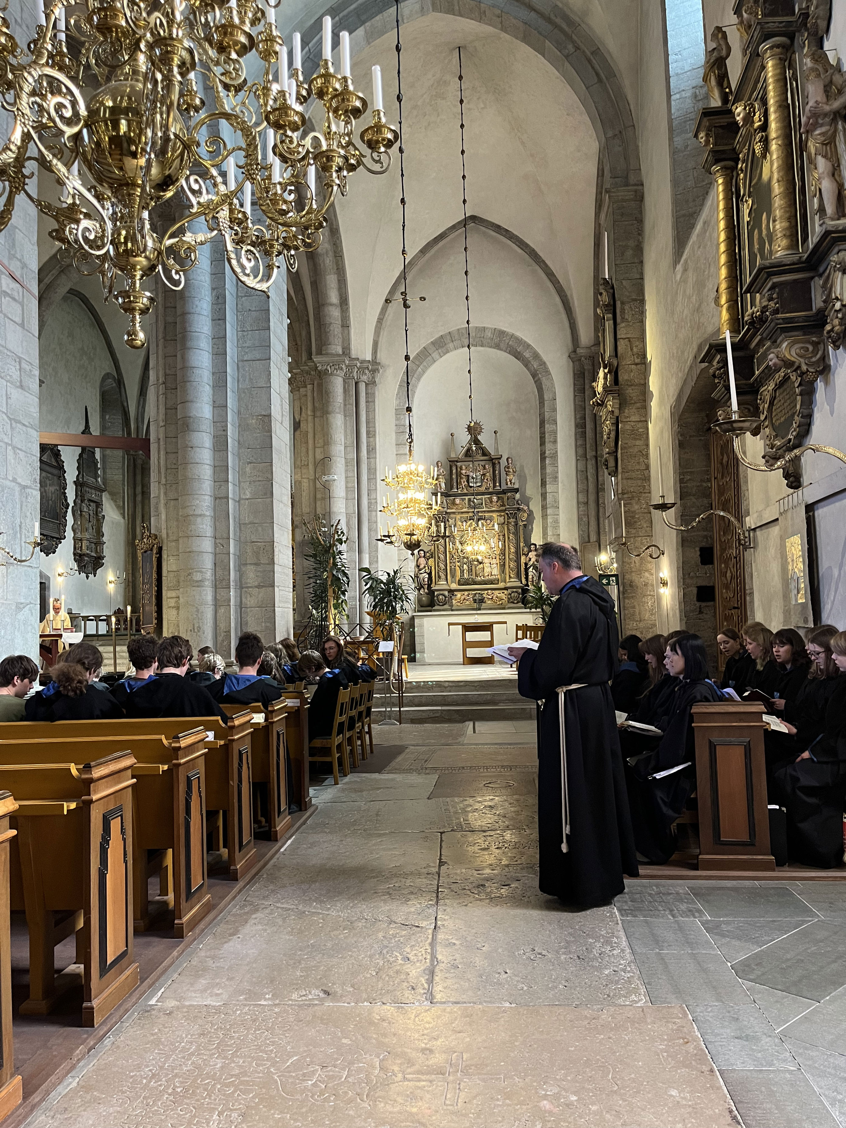 en person i svart kappe som står foran en gruppe mennesker i en kirke