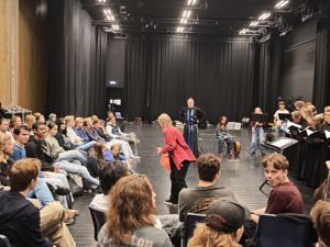 en gruppe mennesker som sitter i et rom med en person som står på en scene